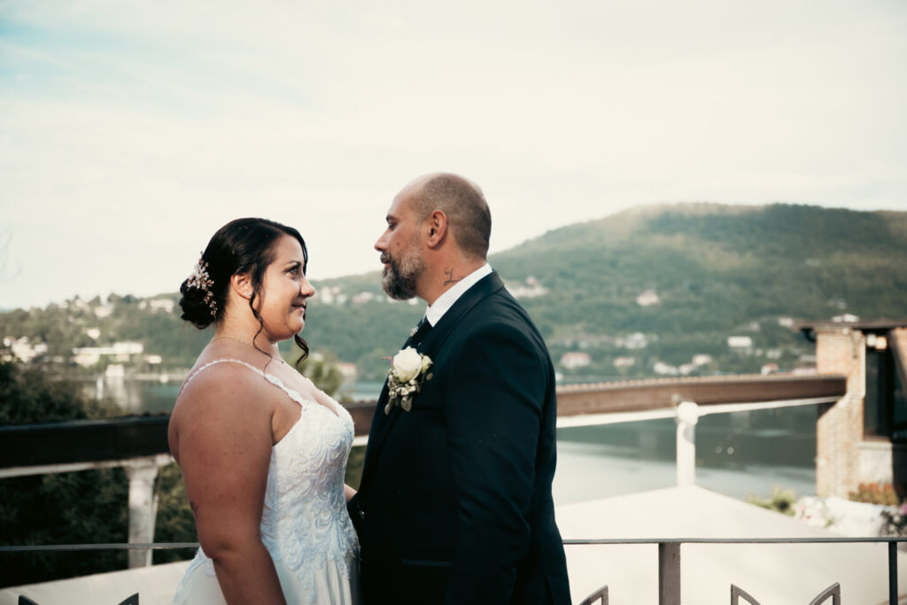 Coppia di sposi che si guarda con complicità davanti a un paesaggio lacustre, durante il loro matrimonio