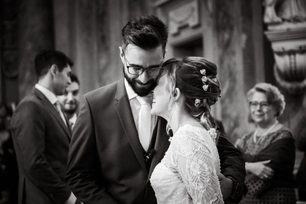 Coppia in bianco e nero, la sposa appoggia sorridendo la fronte sul collo dello sposo, mentre lui guarda in basso emozionato