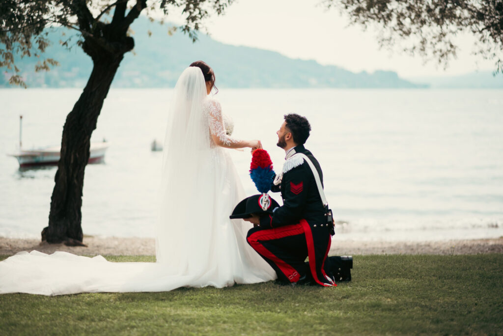 Sposo inginocchiato di spalle che tiene la mano alla sposa, in un momento emozionante durante la cerimonia
