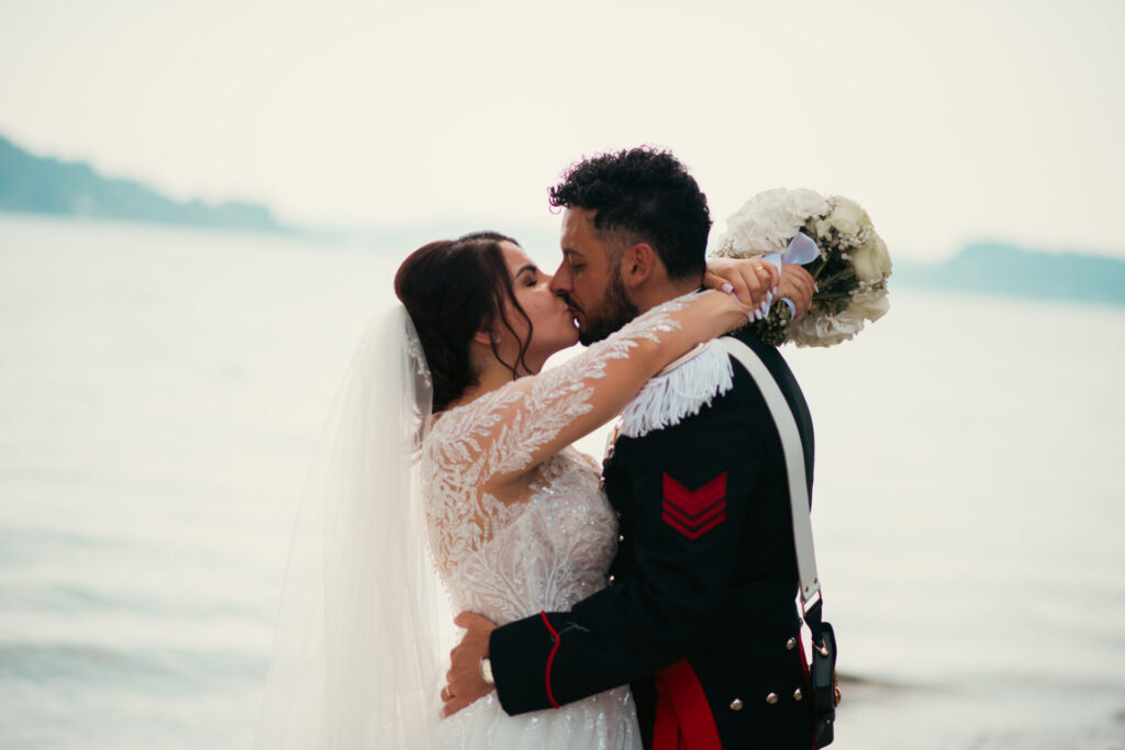 Sposi che si baciano di profilo in un momento intimo durante il loro matrimonio con uno sfondo marino